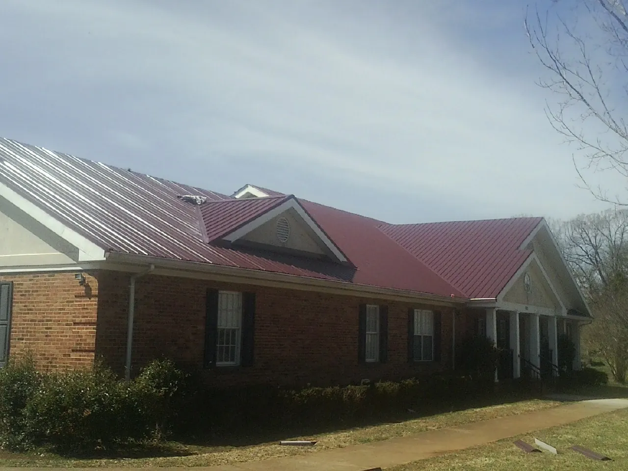 Red metal roof with gabled entries on a long brick building, from a Hail Damage Roof Repair job in Aberdeen